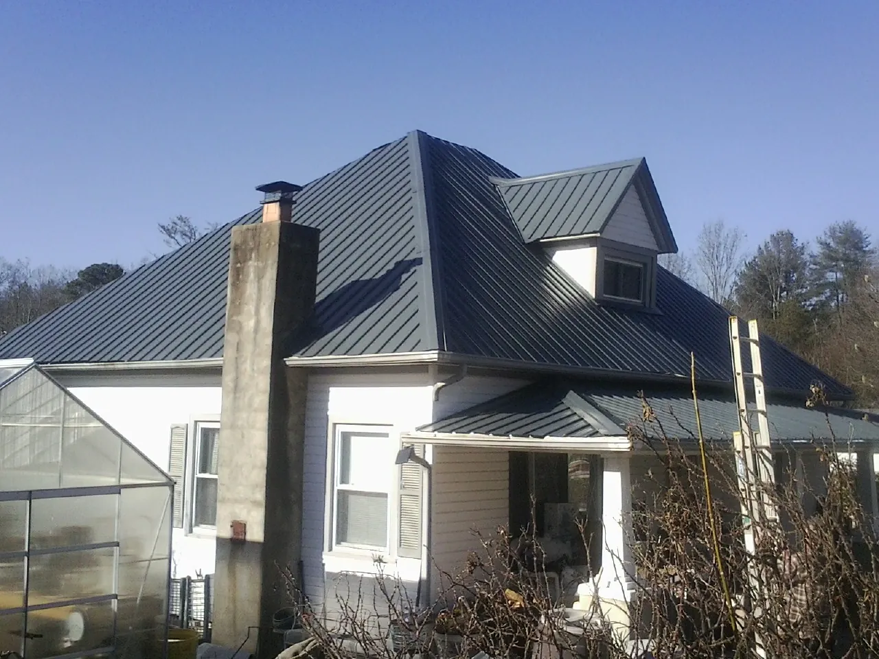 Dark blue standing seam metal roof on a white farmhouse with dormer — Slate & Tile Roof Repair by Roofing Brothers in Emmett