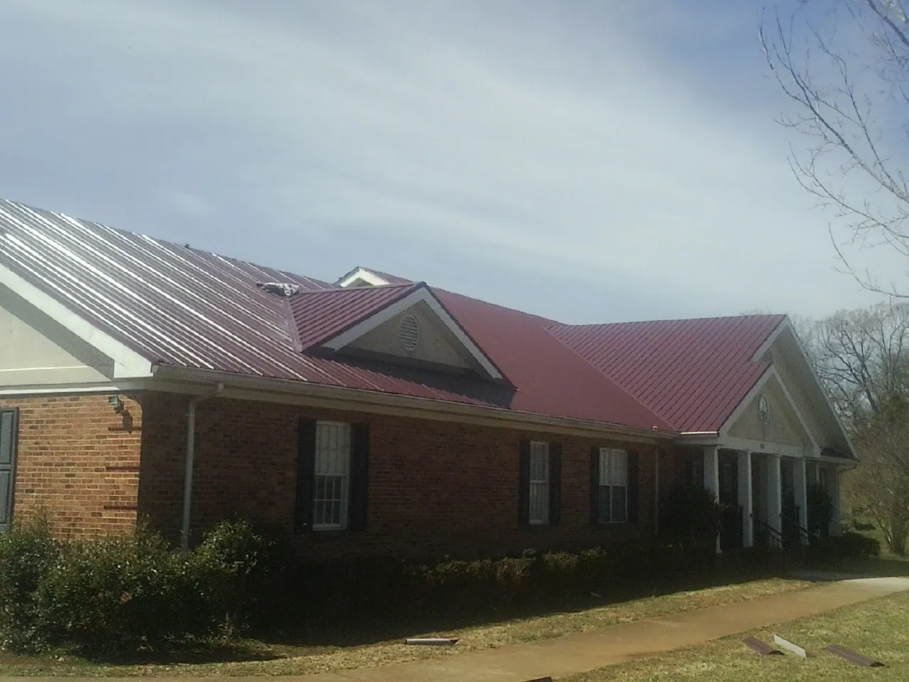 Red metal roof with gabled entries on a long brick building, from a Hail Damage Roof Repair job in Emmett