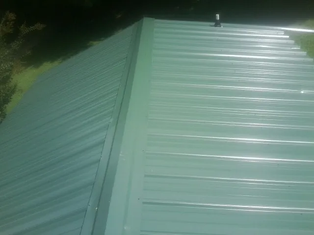 New green metal panels meeting at the ridge of a roof — Flat Roof Repair work by our crew in Emmett