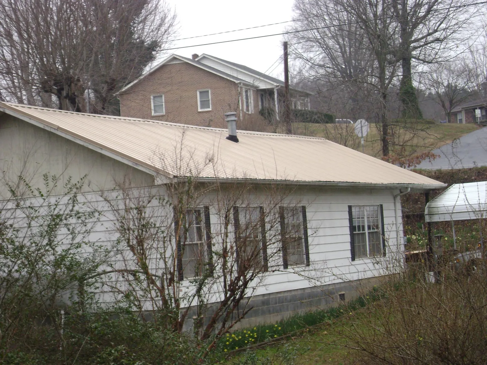 Tan metal roof on a white sided house set into a hillside — Commercial Roofing by Roofing Brothers in Emmett